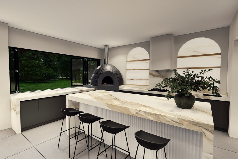 A modern kitchen interior with a large marble-look island, black bar stools, arched niche walls, and a dark freestanding wood-burning oven. Large windows look out onto greenery.